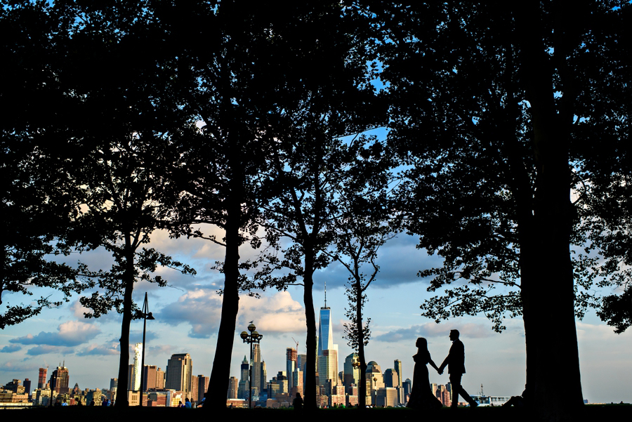 A Silhouette of a couple walking through the trees with the Manhattan Skyline in the background.